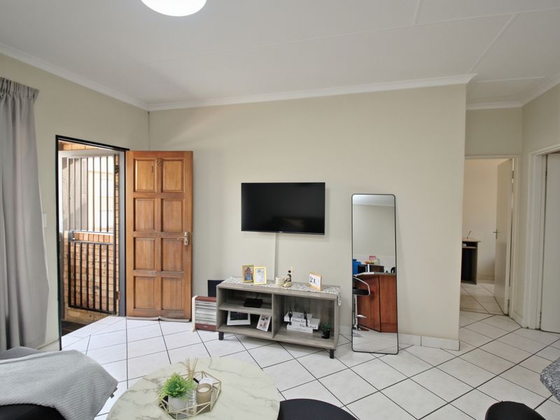 A living room featuring tiled flooring, a timber entrance door with security gate, and neutral wall finishes.