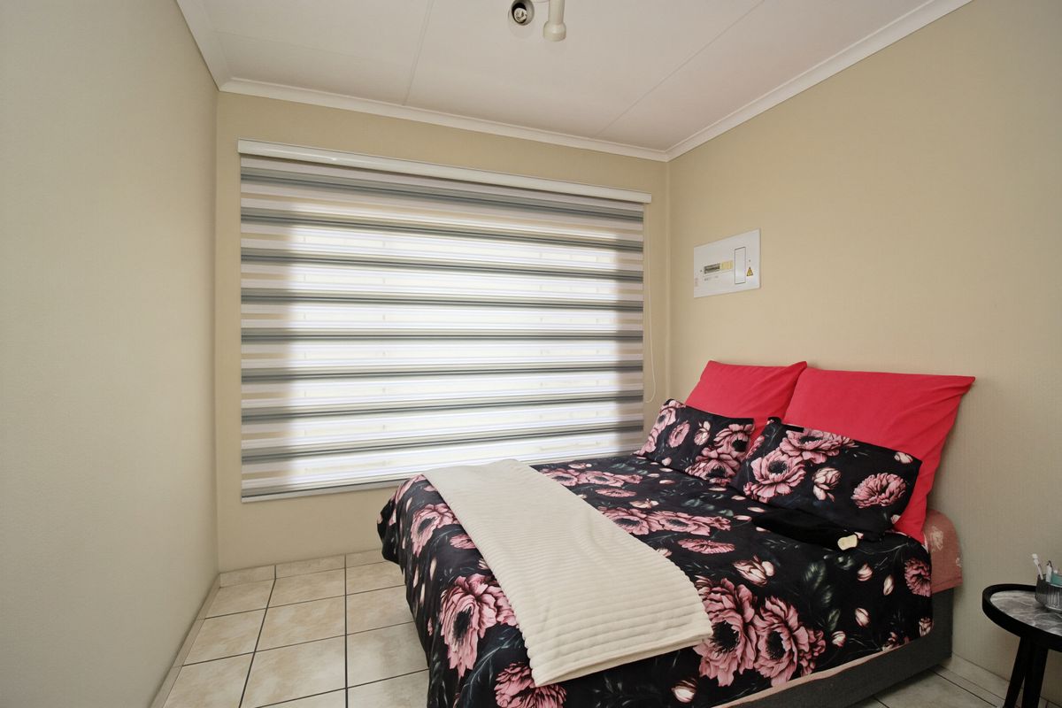 A functional bedroom featuring tiled flooring, neutral wall finishes, and modern zebra blinds for light control.