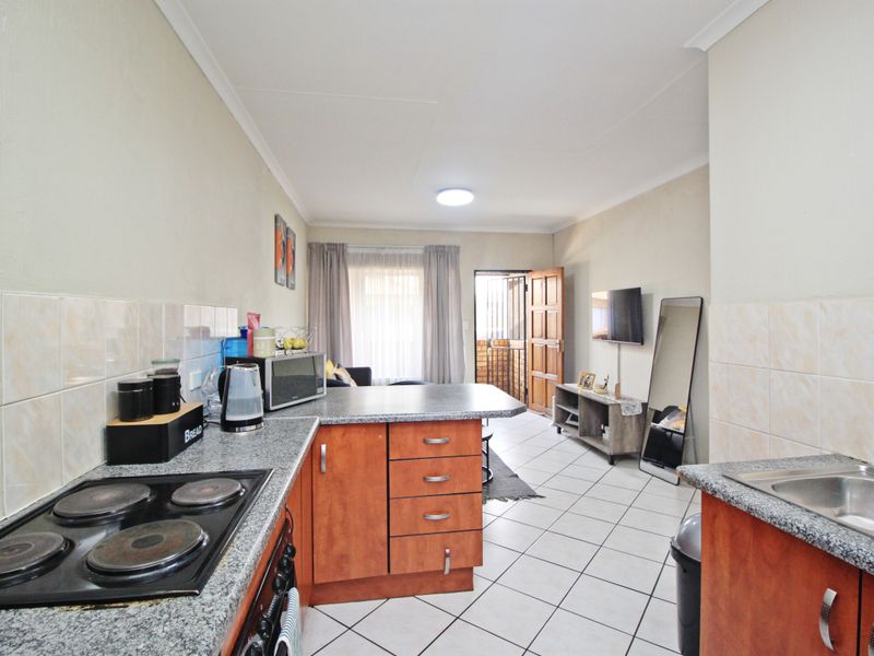 Open-plan kitchen and living area featuring tiled flooring, granite countertops, built-in cabinetry, and an electric hob, leading to an exterior entrance.