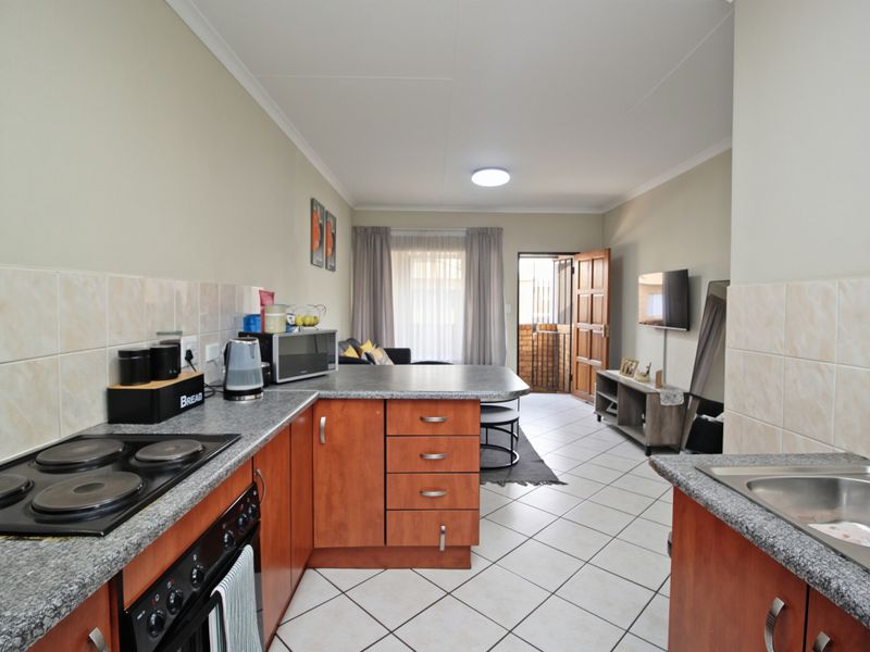 Open-plan kitchen and living area featuring wood-finish cabinetry, laminate countertops, electric hob, and tiled flooring leading to an exterior entrance.