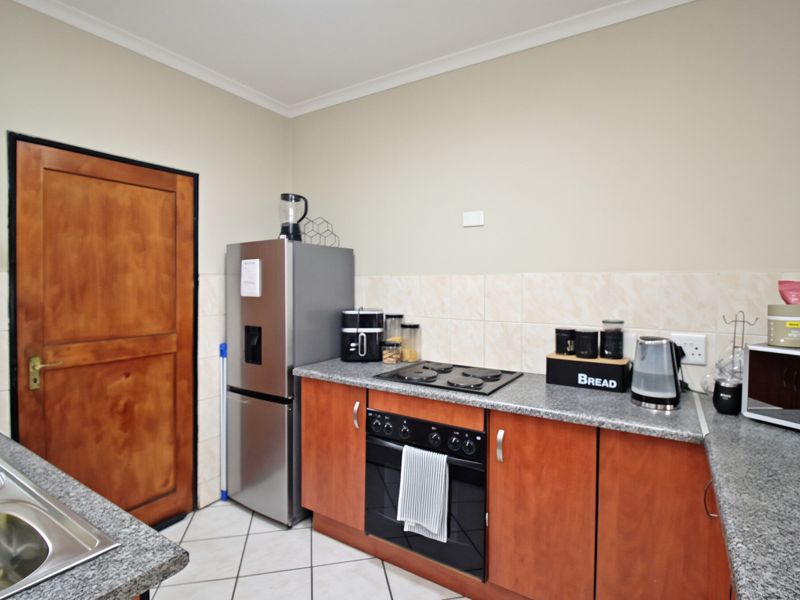 Functional kitchen featuring laminate cabinetry, granite countertops, built-in oven, electric hob, and tiled backsplash with ceramic flooring.