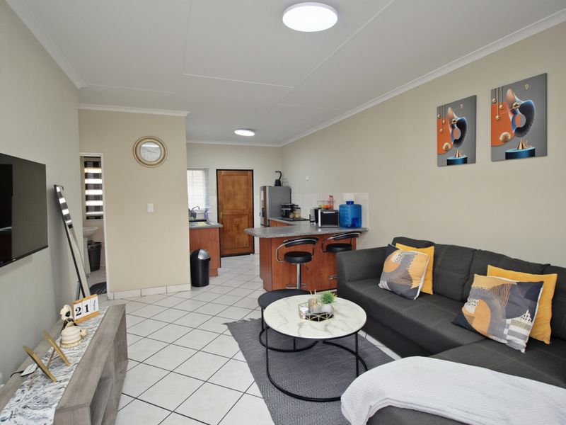 Open-plan living area featuring tiled flooring, a compact kitchen with breakfast bar, and direct access to adjacent rooms.
