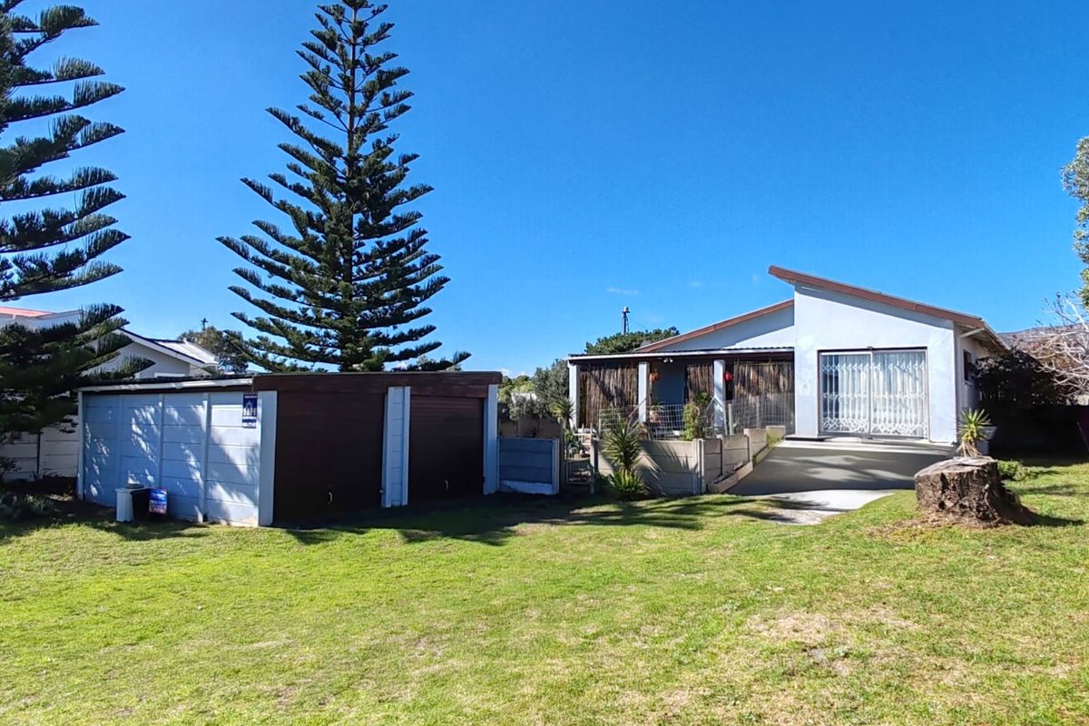 Rear view of the property featuring a double garage, concrete driveway, and a lawn area with a large tree.