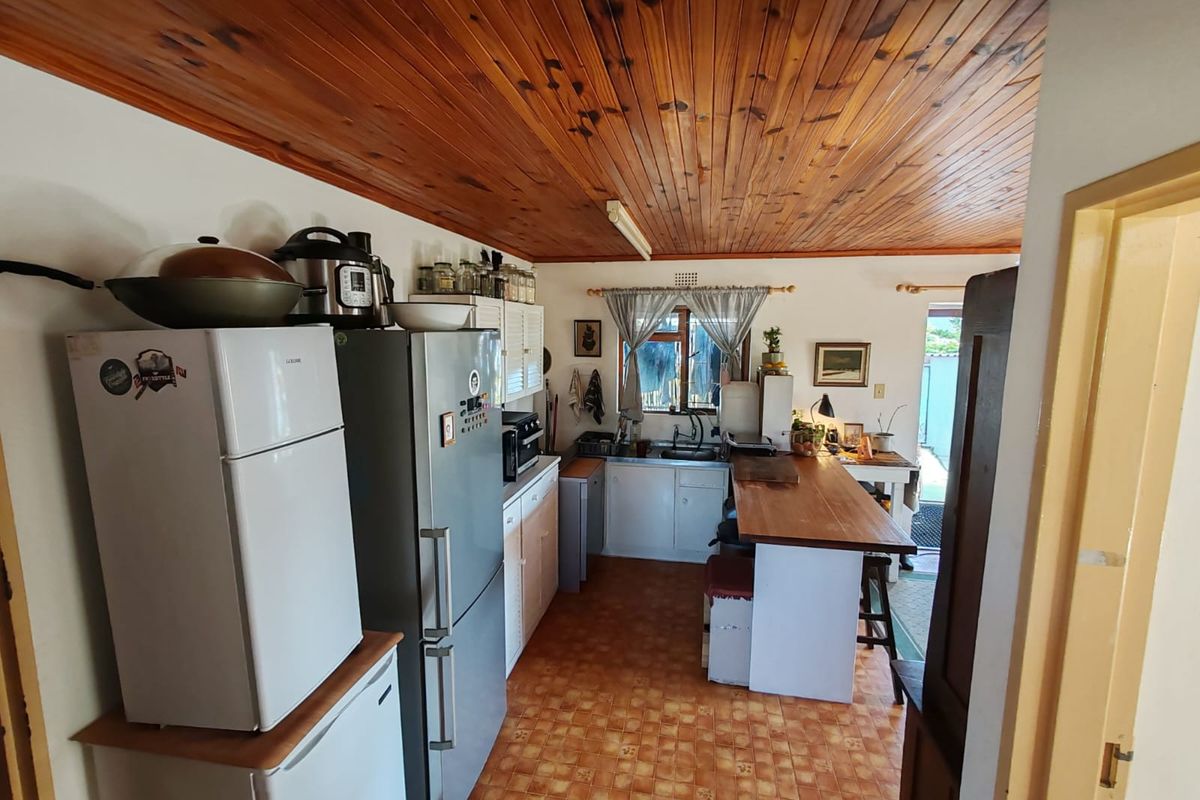A functional kitchen featuring timber tongue and groove ceilings, tiled flooring, and a built-in breakfast bar with direct access to the exterior.