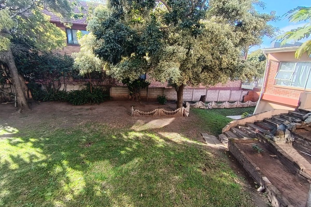 A rear garden area featuring mature trees, a brick boundary wall, and stone-stepped access leading to the townhouse structure.