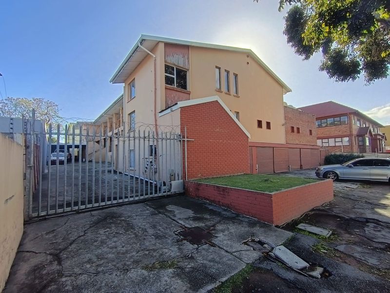 Exterior view of a townhouse complex featuring a concrete driveway, security fencing with razor wire, and multiple roller shutter garage doors.