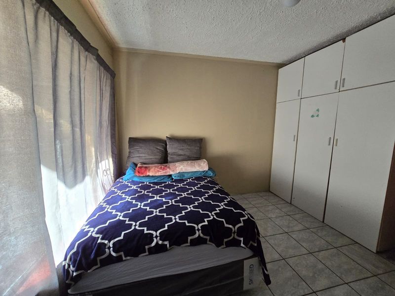 A bedroom featuring built-in cupboards, tiled flooring, and natural light from the window. The room offers functional storage and a neutral layout.