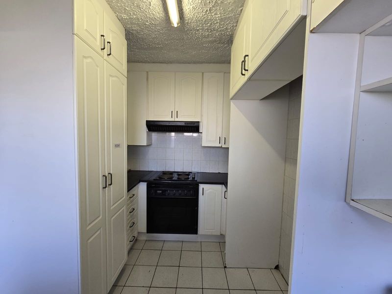 A functional kitchen featuring built-in cabinetry, an electric hob, oven, extractor fan, and tiled flooring, offering a clean and practical layout.