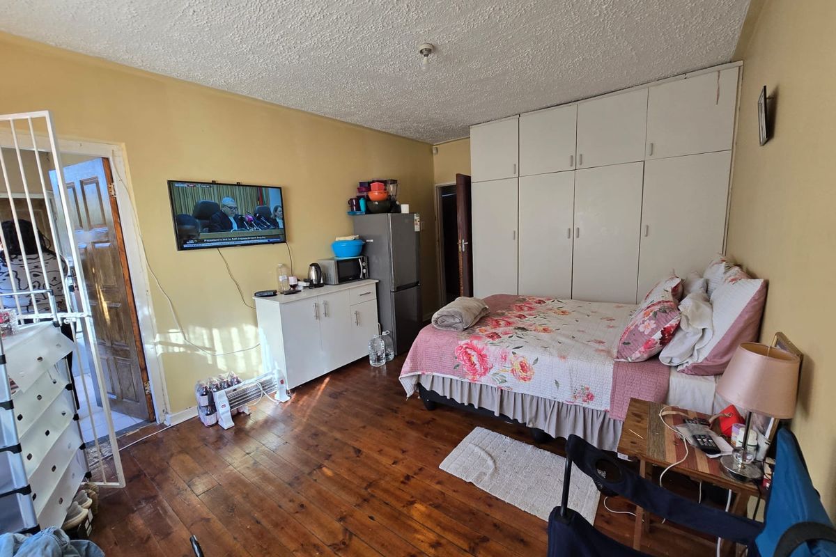 A bedroom featuring timber flooring, built-in cupboards, and a security gate at the entrance.