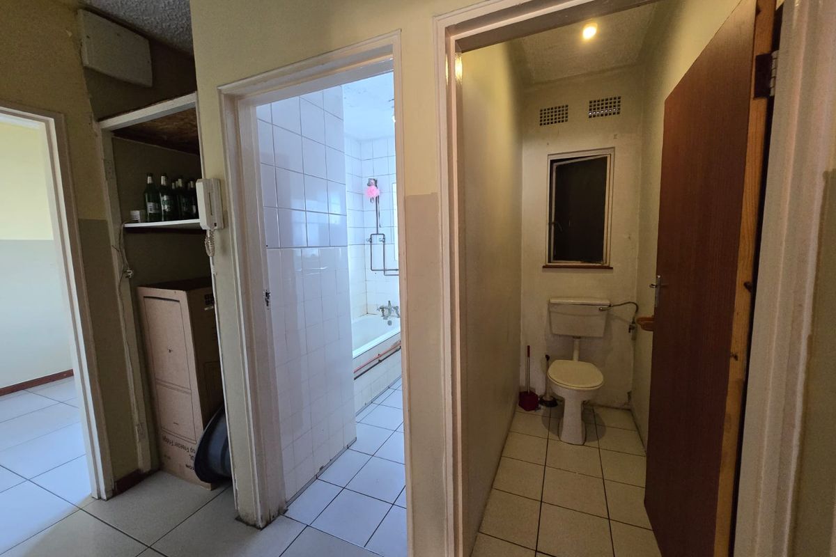 A functional bathroom and separate toilet area featuring tiled surfaces and basic fixtures, currently in need of cosmetic updates and modernization.