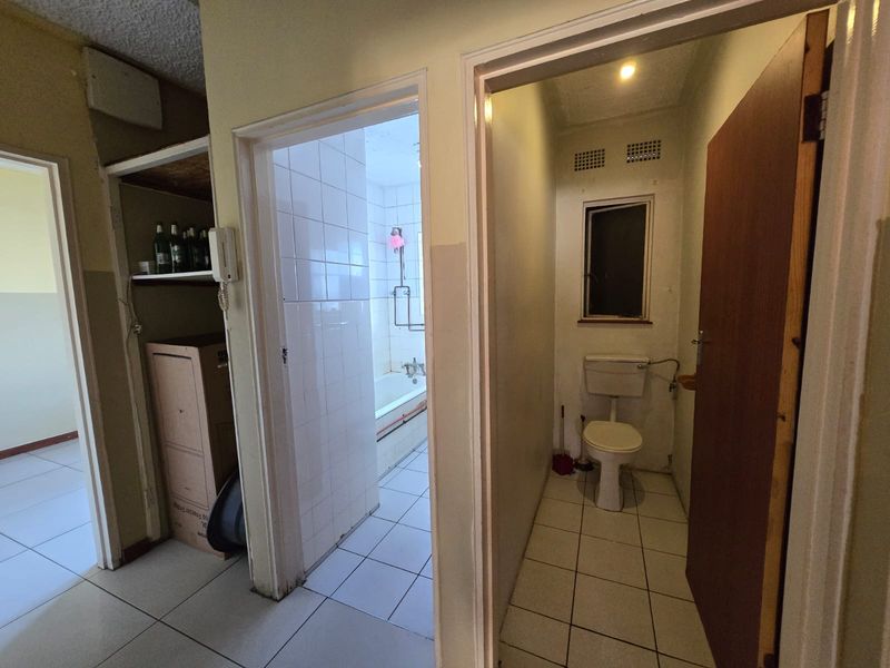 A functional bathroom and separate toilet area featuring tiled surfaces and basic fixtures, currently in need of cosmetic updates and modernization.