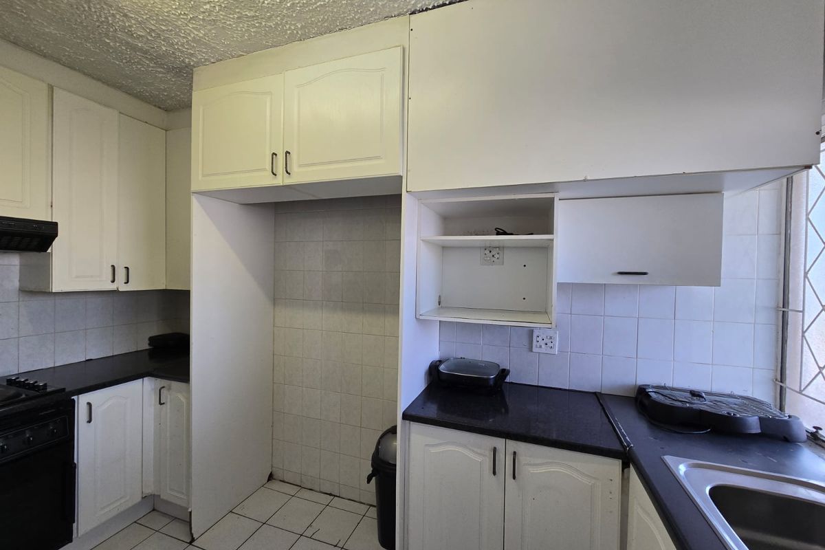 A functional kitchen featuring white cabinetry, dark countertops, tiled backsplash, and built-in oven with extractor fan, offering potential for modern updates.