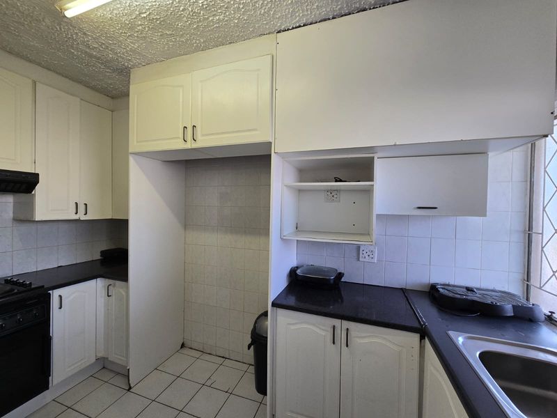 A functional kitchen featuring white cabinetry, dark countertops, tiled backsplash, and built-in oven with extractor fan, offering potential for modern updates.