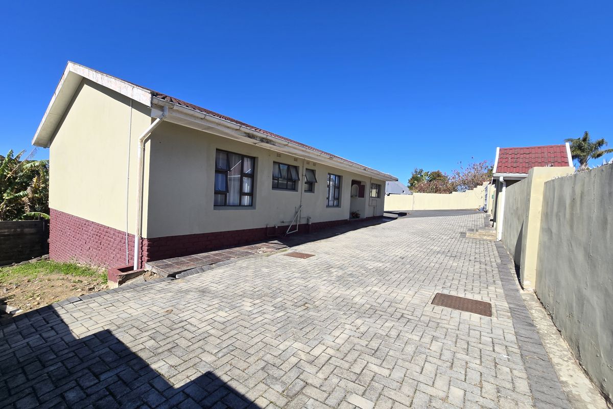 A view of the rear exterior of the house featuring a paved driveway, perimeter wall, and tiled roof structure.