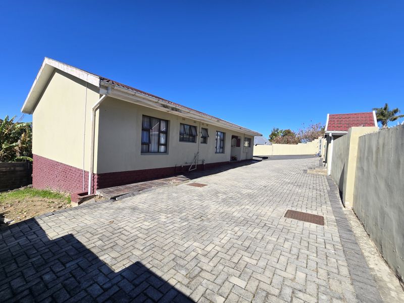 A view of the rear exterior of the house featuring a paved driveway, perimeter wall, and tiled roof structure.