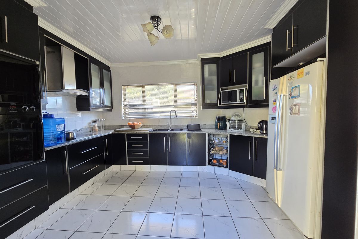 A functional kitchen featuring dark cabinetry, granite countertops, tiled flooring, and a tongue and groove ceiling with integrated lighting.