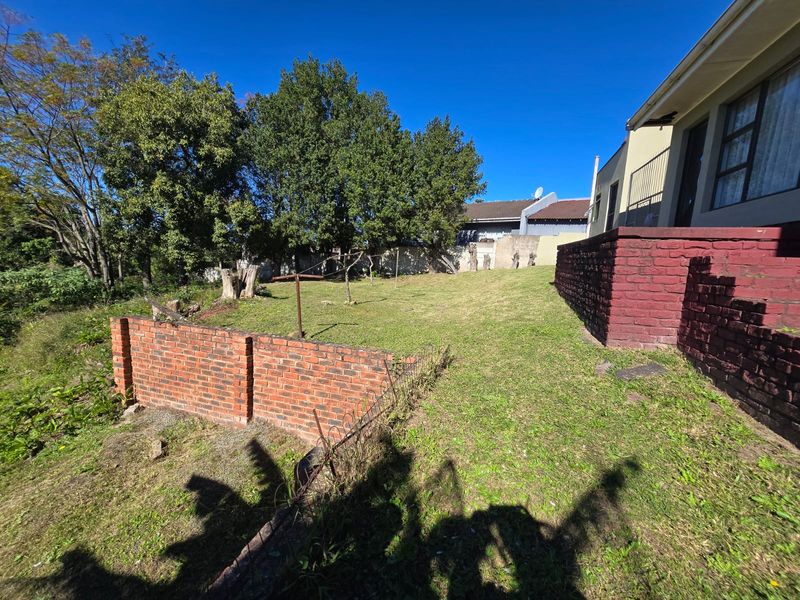 A rear garden area featuring a lawn, brick retaining walls, and a metal clothesline, adjacent to the main house structure.