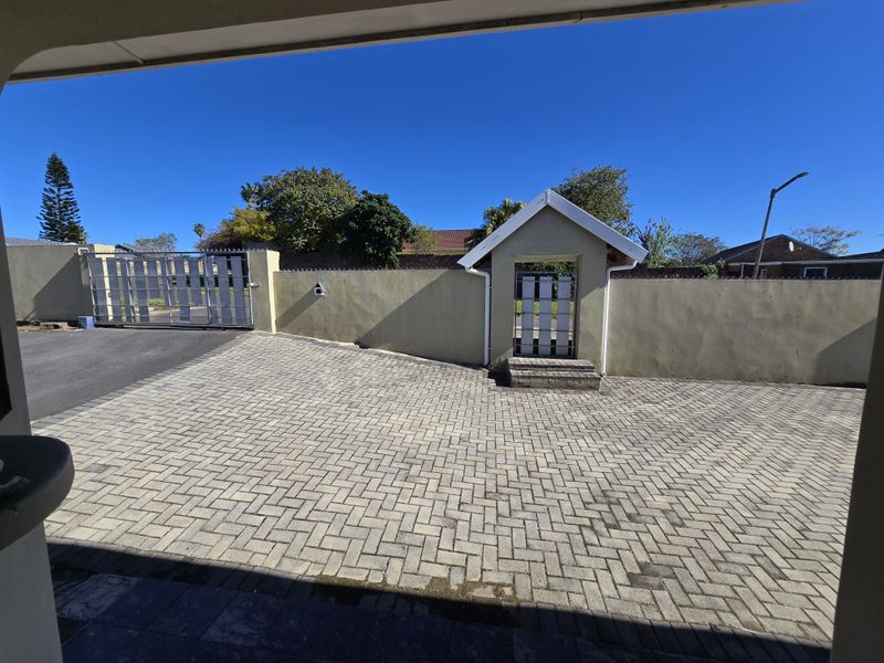 A paved front driveway featuring a secure boundary wall, a pedestrian gate with a small roof structure, and a sliding vehicle gate.