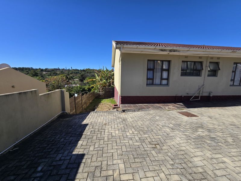 Rear exterior view of the property featuring a paved driveway, boundary wall, and tiled roof structure with established garden surroundings.
