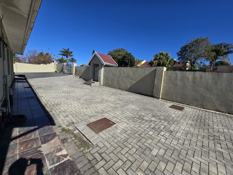A paved rear driveway area featuring a boundary wall, drainage access points, and a small detached outbuilding structure.