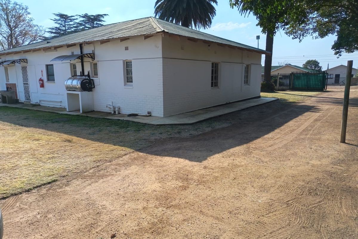Rear view of a single-story house featuring white painted brick walls, a corrugated metal roof, and an external geyser unit.