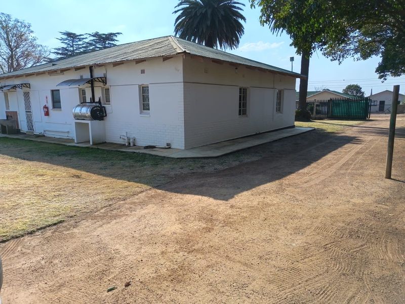 Rear view of a single-story house featuring white painted brick walls, a corrugated metal roof, and an external geyser unit.