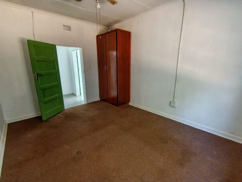 A simple bedroom featuring a built-in wardrobe, ceiling fan, and carpeted flooring, presenting a blank canvas for potential renovation or restyling.