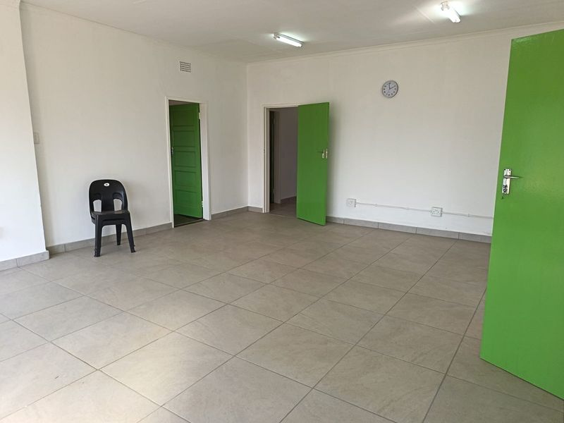 An empty, neutrally painted living area featuring large format floor tiles and multiple internal access points.