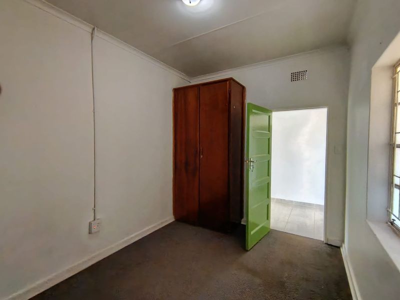 A simple bedroom featuring a built-in wardrobe, carpeted flooring, and a green security door leading to an adjacent space.