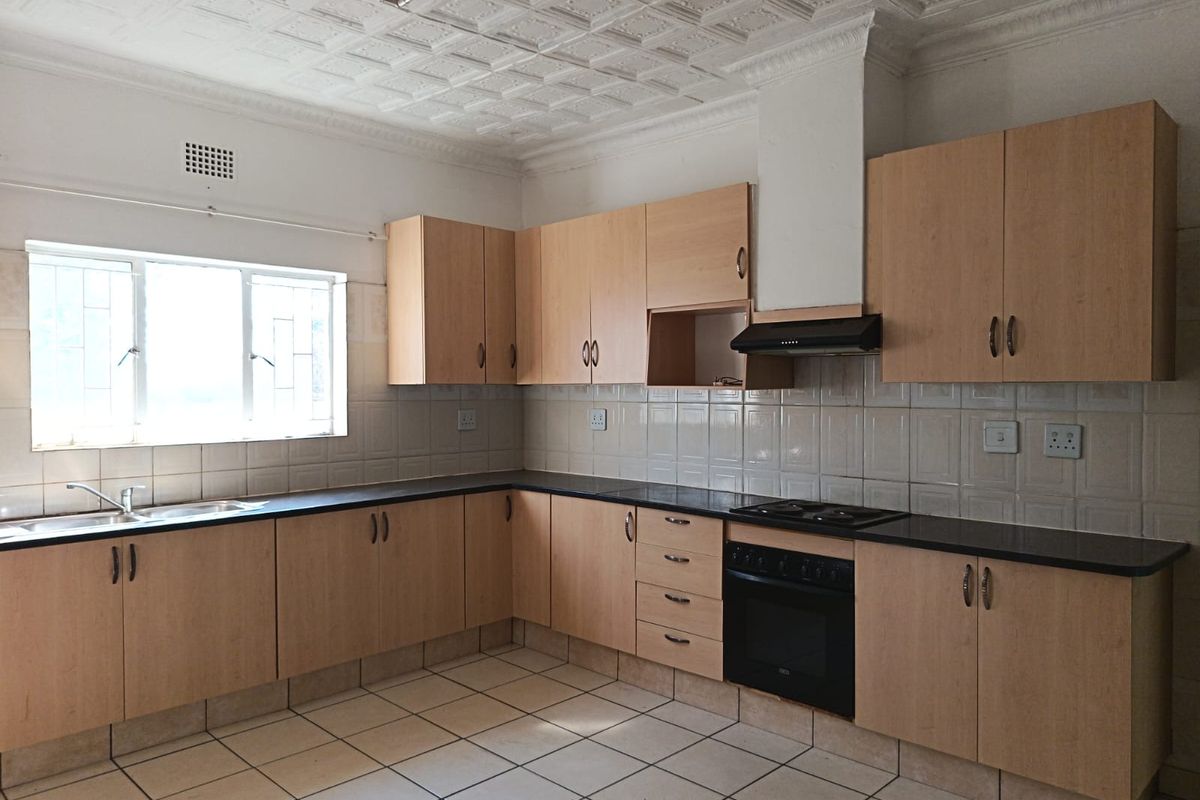 A functional kitchen featuring laminate cabinetry, built-in oven with hob, tiled splashbacks, and decorative ceiling tiles, offering a clean canvas for modern updates.