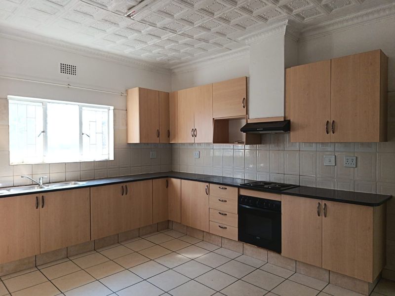 A functional kitchen featuring laminate cabinetry, built-in oven with hob, tiled splashbacks, and decorative ceiling tiles, offering a clean canvas for modern updates.