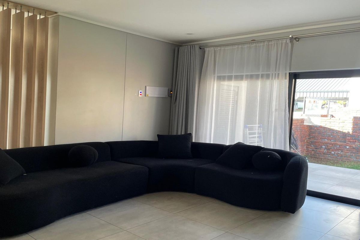 Modern living room featuring large format floor tiles, a timber slat room divider, and a sliding glass door providing access to the outdoor area.