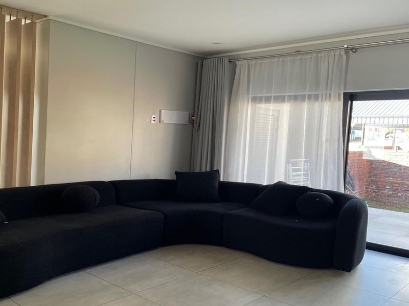 Modern living room featuring large format floor tiles, a timber slat room divider, and a sliding glass door providing access to the outdoor area.