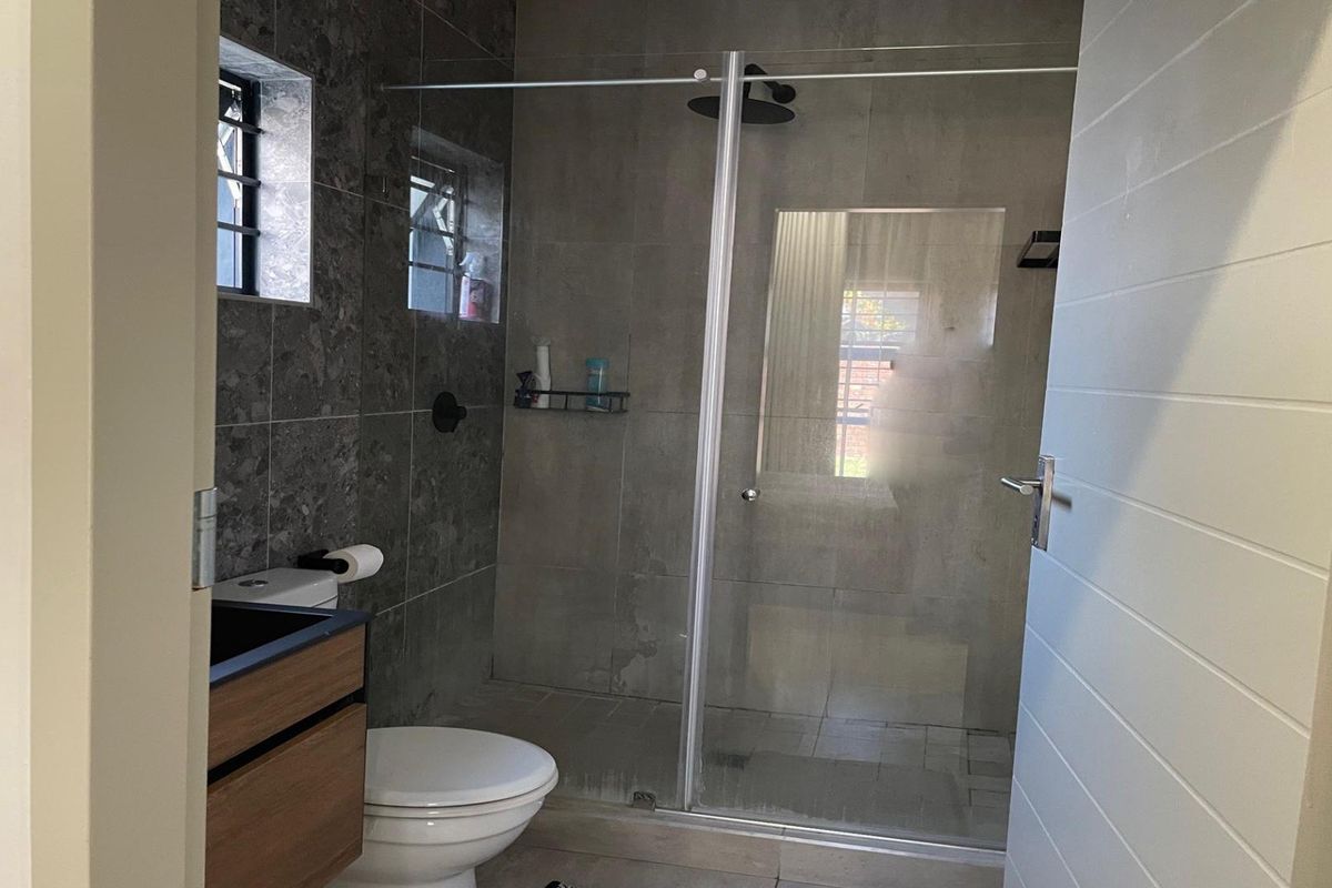 Modern bathroom featuring a walk-in shower with a glass screen, rain shower head, wall-mounted toilet, and a contemporary vanity cabinet.