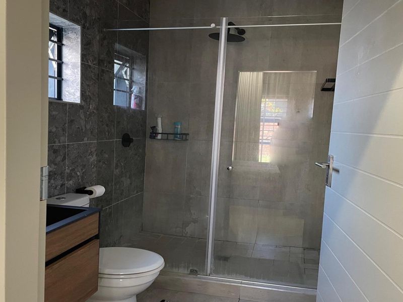 Modern bathroom featuring a walk-in shower with a glass screen, rain shower head, wall-mounted toilet, and a contemporary vanity cabinet.