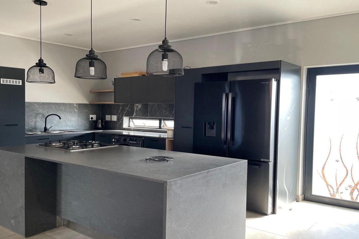 Modern kitchen featuring dark matte cabinetry, a central island with a gas hob, stone countertops, and stylish pendant lighting with direct outdoor access.