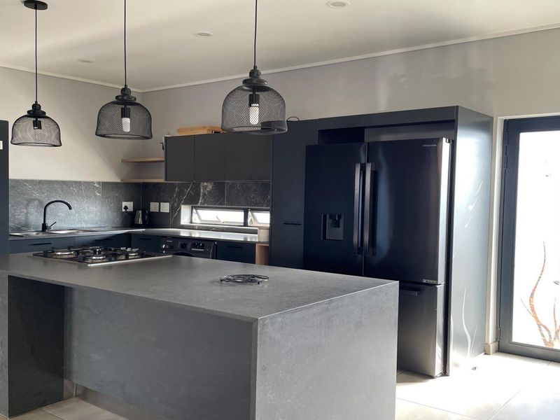 Modern kitchen featuring dark matte cabinetry, a central island with a gas hob, stone countertops, and stylish pendant lighting with direct outdoor access.