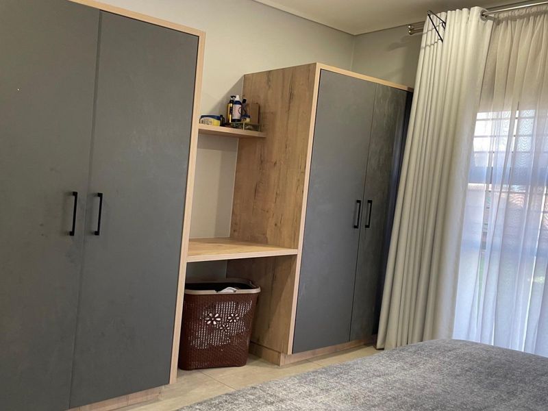 A bedroom featuring modern built-in cupboards with a central integrated desk area and large window with curtain rails.