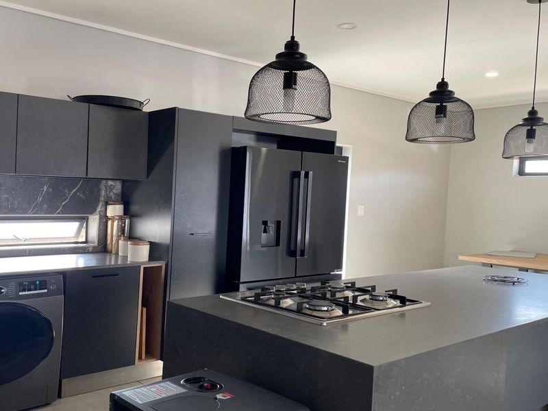 Modern kitchen featuring dark cabinetry, a central island with a gas hob, stone countertops, and integrated appliances in a sleek, contemporary design.