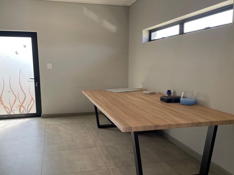 A modern, minimalist office space featuring neutral walls, large format floor tiles, a sleek desk, and a frosted glass door with natural light.