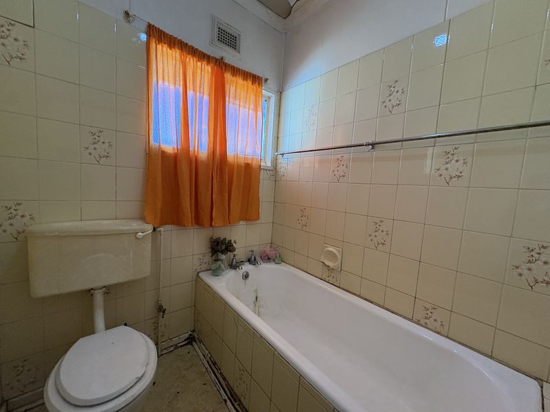 A dated bathroom featuring a built-in bathtub, toilet, and original ceramic wall tiles, offering significant potential for a modern renovation.