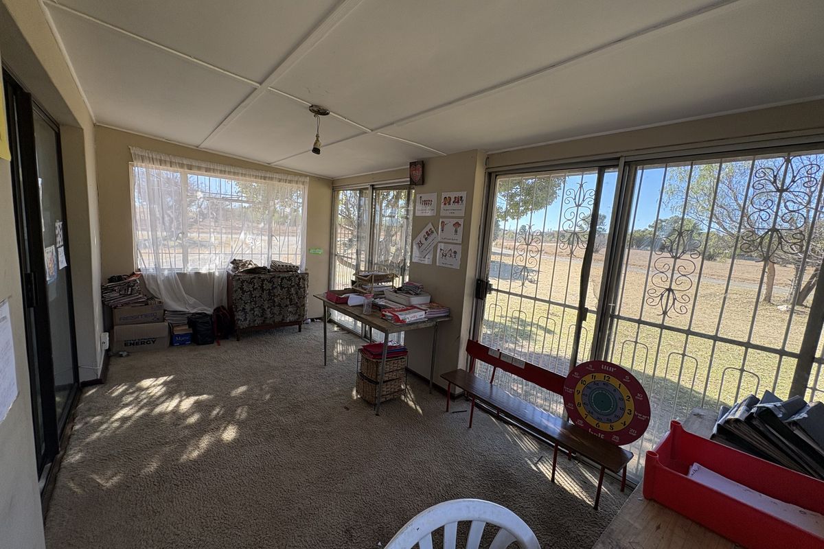 A sunlit living area featuring large sliding glass doors with security gates, carpeted flooring, and an exposed beam ceiling, offering views of the exterior.