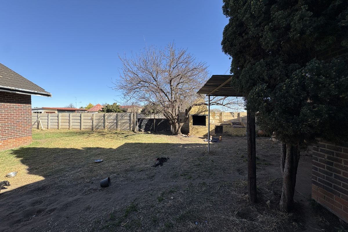 Rear garden area featuring a brick braai, covered patio structure, and perimeter precast concrete walling.