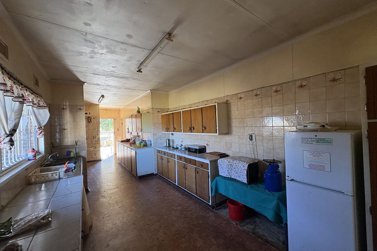 A spacious, dated kitchen featuring extensive built-in cabinetry, tiled splashbacks, and a functional layout with direct access to the exterior.