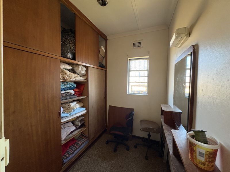 A compact bedroom featuring extensive built-in wooden cabinetry, a wall-mounted air conditioning unit, and a louvered window for natural ventilation.
