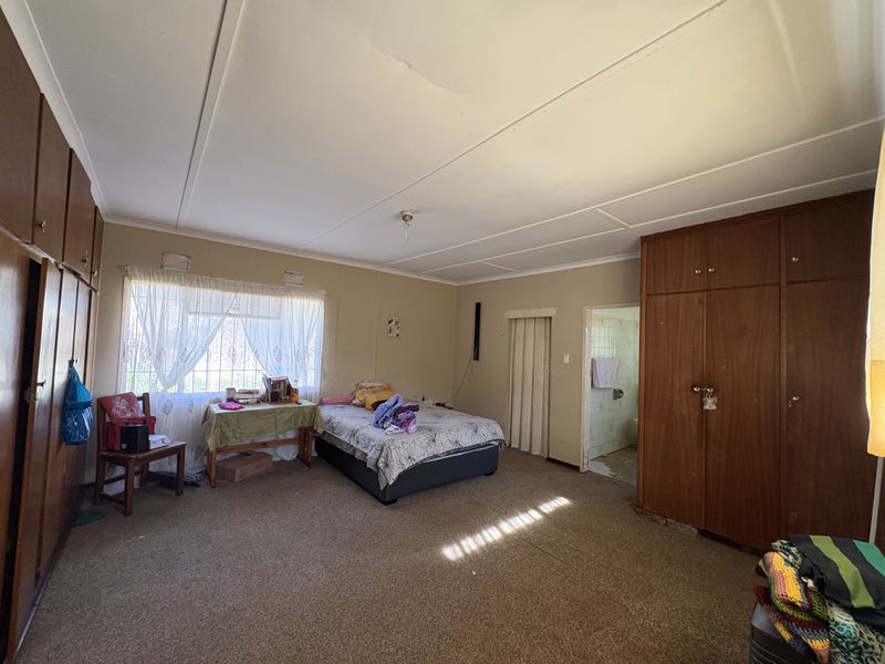 Spacious bedroom featuring built-in wooden cupboards, carpeted flooring, and an en-suite bathroom access point. The room requires cosmetic updates to modernize the finishes.