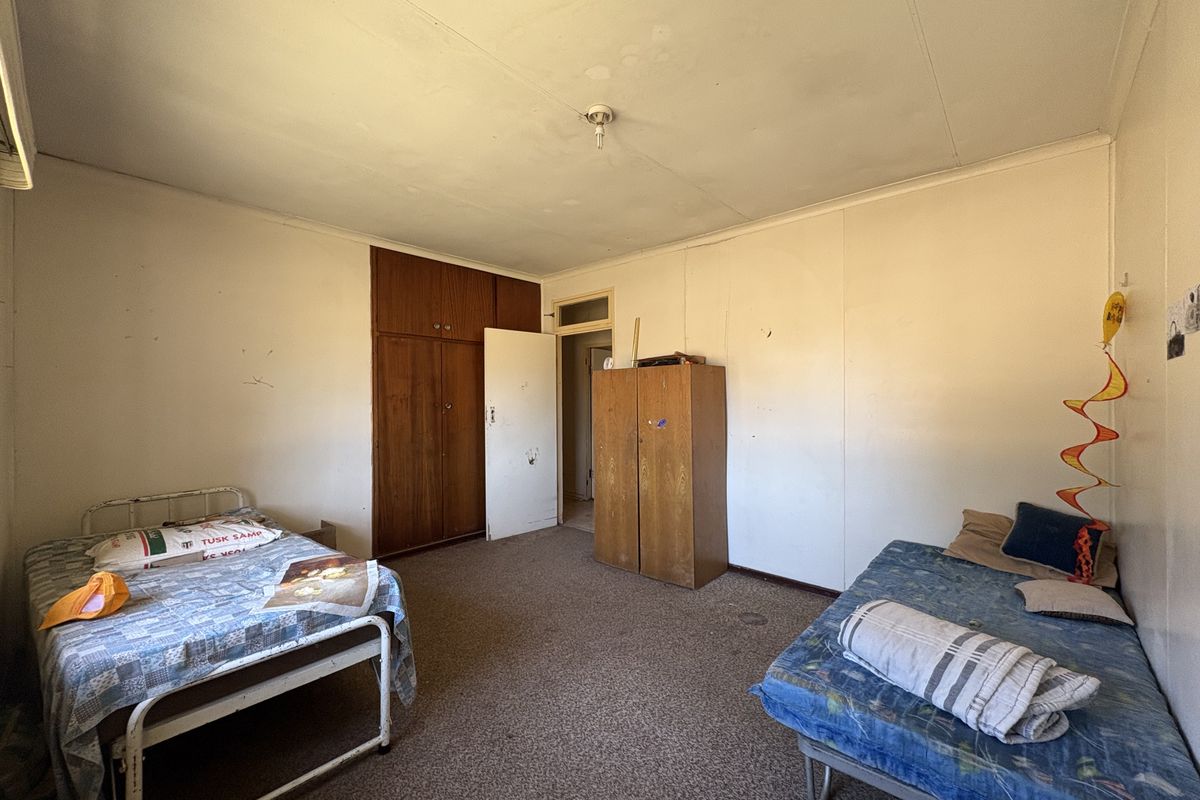 A bedroom featuring a built-in wooden wardrobe, carpeted flooring, and standard wall finishes, requiring cosmetic updates to improve its overall condition.