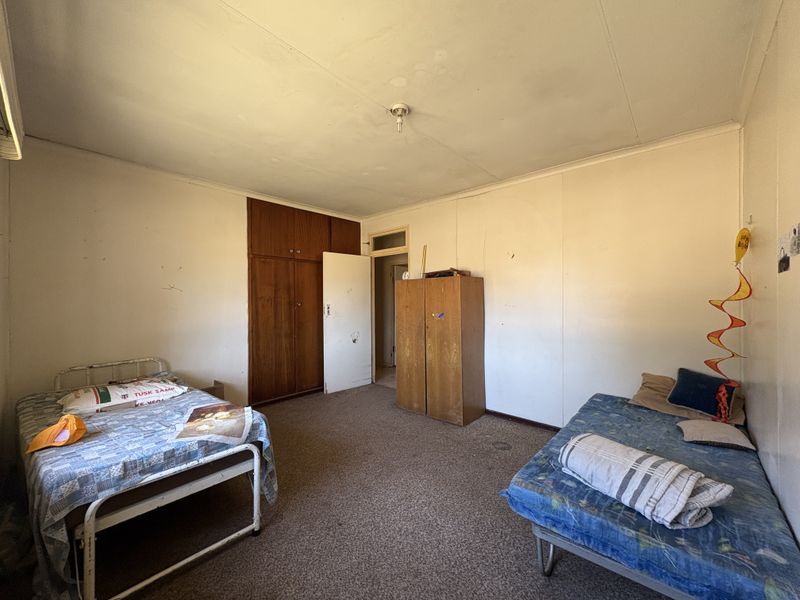 A bedroom featuring a built-in wooden wardrobe, carpeted flooring, and standard wall finishes, requiring cosmetic updates to improve its overall condition.