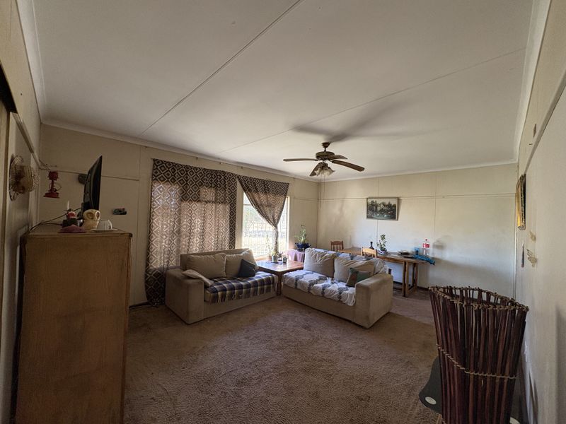 A spacious living room featuring a ceiling fan and carpeted flooring, offering a blank canvas for potential modernization and interior updates.
