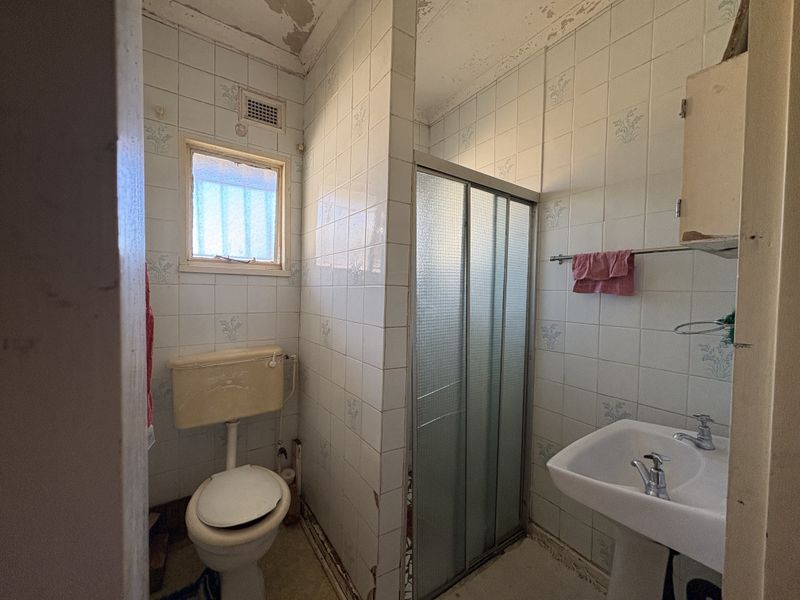 A dated bathroom featuring a pedestal basin, shower enclosure, and toilet, requiring significant renovation and cosmetic updates to improve its condition.